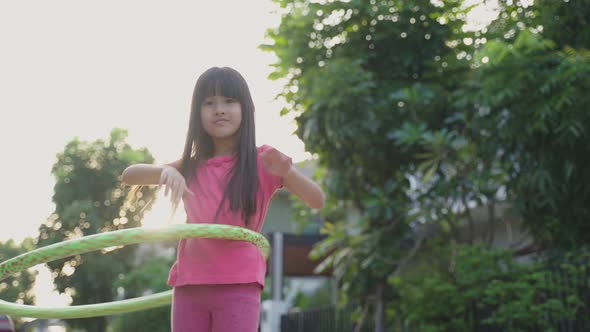 Young Asian little girl playing hulahoop exercise outdoor at home for health care and wellbeing. alt