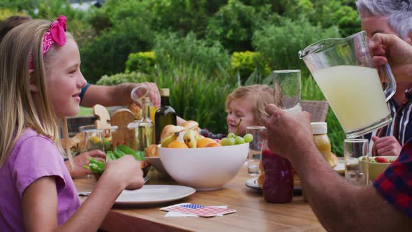 Smiling caucasian girl drinking lemonade at family celebration meal in garden alt