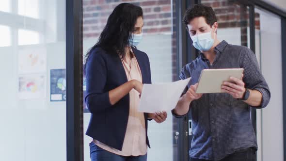 Man and woman wearing face masks discussing at office alt