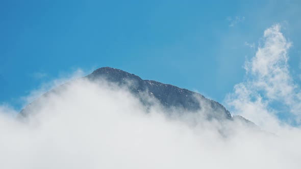 High Steep Rocky Mountain Ridge on Blue Sky Background Surrounded By Moving Clouds alt