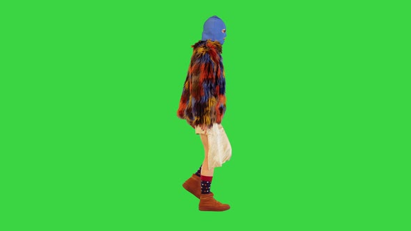 Caucasian Girl in Balaclava and Multicolored Fur Coat Walks on a Green Screen Chroma Key