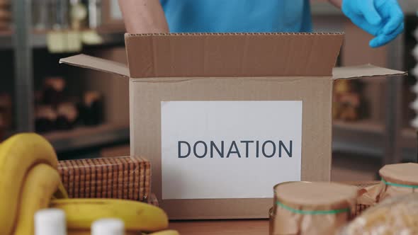 Close Up of Volunteer in Gloves Packing Food in Donation Box alt