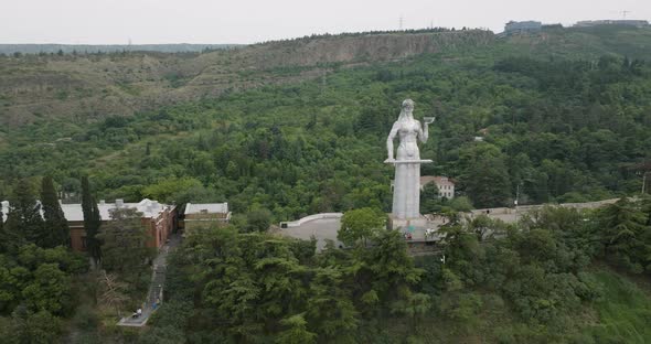 Arc aerial shot of the Kartlis Deda statue and a beautiful Tbilisi landscape. alt