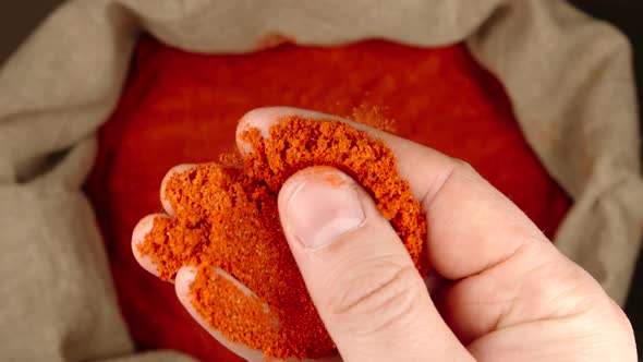 Human hand holds and touches a pinch of red pepper powder over a sac
