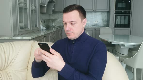 young adult man relaxing on comfortable couch, using mobile application in living room alt