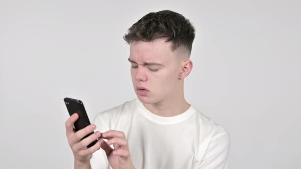 Young Man Reacting To Loss and Using Smartphone on White Background alt