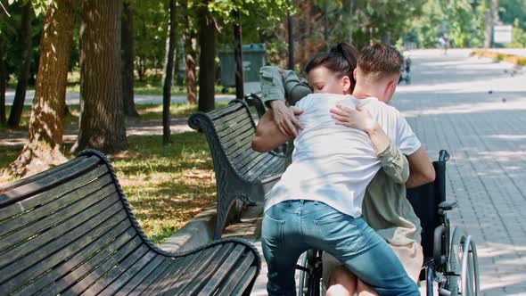 A Guy Helping Disabled Woman to Sit on a Bench From Her Wheelchair alt