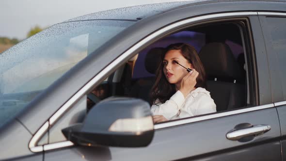 Brunette Applying Mascara to the Car Front Mirror and Smiling at Camera alt