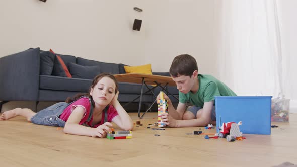 Girl and a boy playing and constructing with toy bricks on the living room floor alt