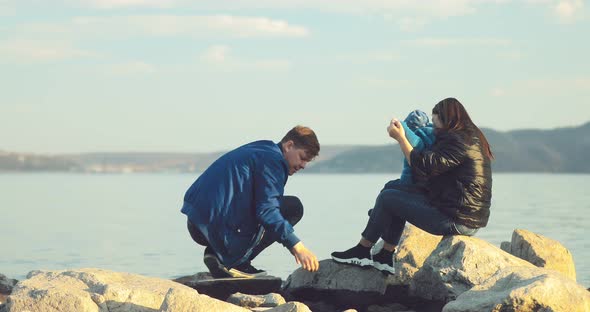 Man with His Family Sits on the Beach on Large Stones and Throws Stones Into the Water alt