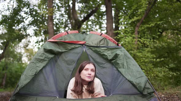 Portrait of a Tourist Woman Peeking Out of a Green Tent in the Woods in Nature