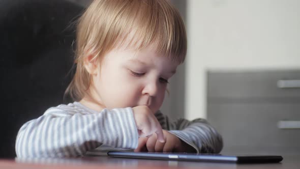 Portrait of Toddler Sitting at Desk and Tapping Screen of Digital Tablet