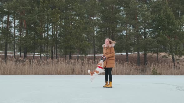 A girl in a coat and yellow boots plays in the winter on the ice of the lake with a dog alt