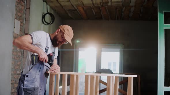 Male Construction Worker Screws Screws Into a Wooden Structure in the Studio