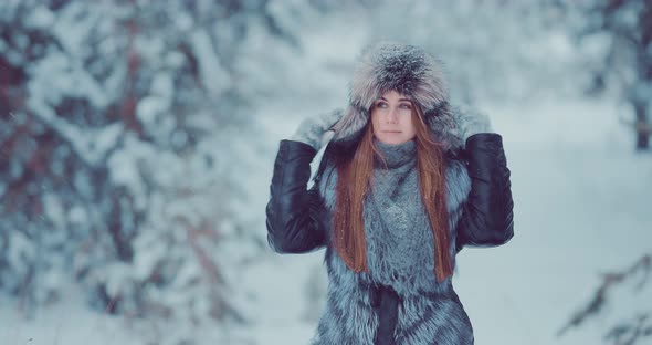 Beautiful Girl in a Fur Hat and Jacket Walks in the Park in Winter alt