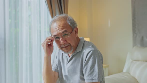 Portrait of Happy Asian Senior elderly grandfather sit on sofa at home put eyeglasses on his face. alt