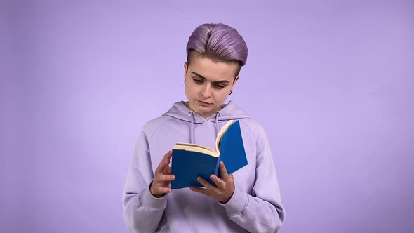 Female Student Turning Pages Reading Book Isolated on Purple Indoors alt