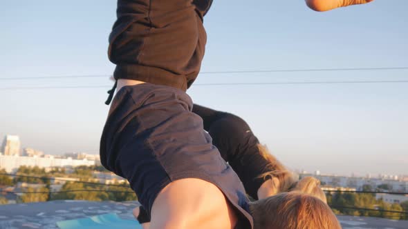 Young Beautiful Guy and Yoga Girl Perform Exercises on the Roof Against the Background of the City