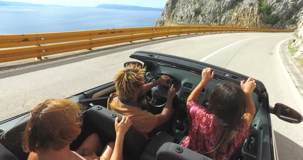 Friends having fun driving on the road along the coast in red convertible alt