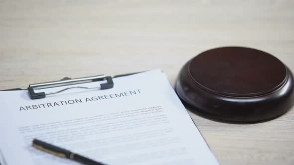 Arbitration Agreement Document on Table, Gavel Striking on Sound Block, Dispute alt