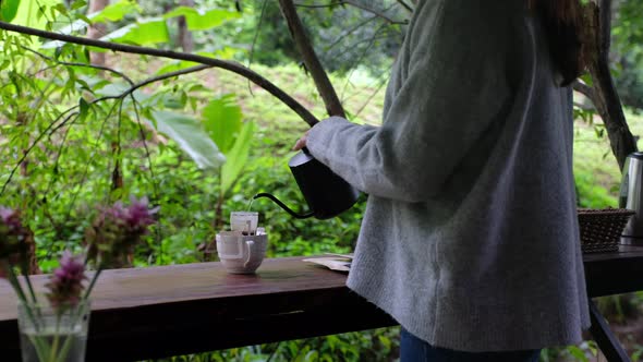 a woman pouring hot water from kettle to make drip coffee