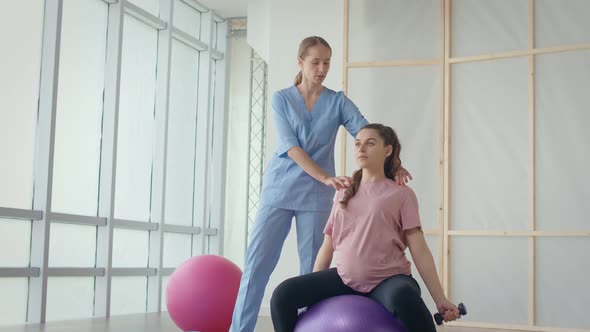A Health Worker at a Medical Center Helps a Pregnant Woman to Do Exercises alt