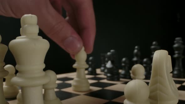 Man's Hand Moving White Bishop Chess Piece From First Line alt