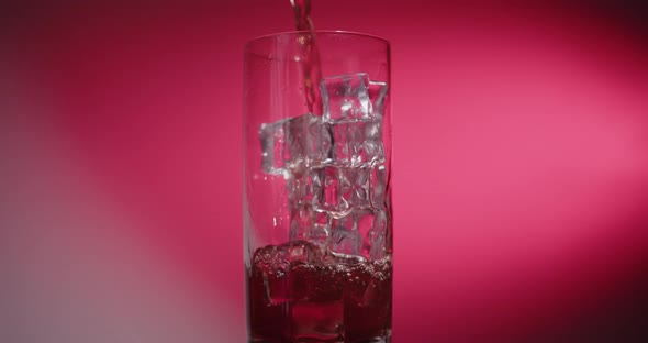 Red drink is poured into a glass with ice cubes (Clip for product videos) alt