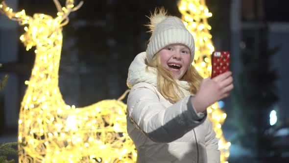Beautiful Blonde Takes Selfie with Smartphone on Christmas Decorated Street in Winter
