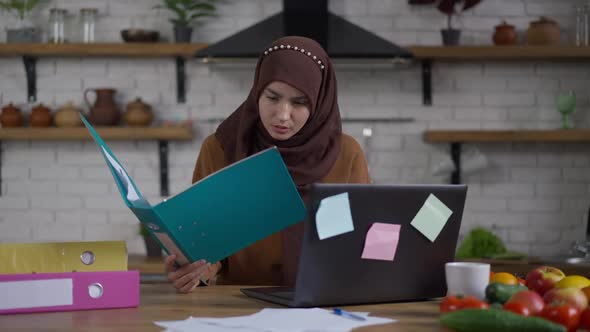 Focused Concentrated Woman in Hijab Comparing Documents and Online Information on Laptop alt