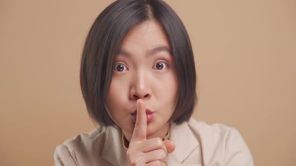 Close up shot of Asian business woman putting index finger on lips meaning keeping secret isolated