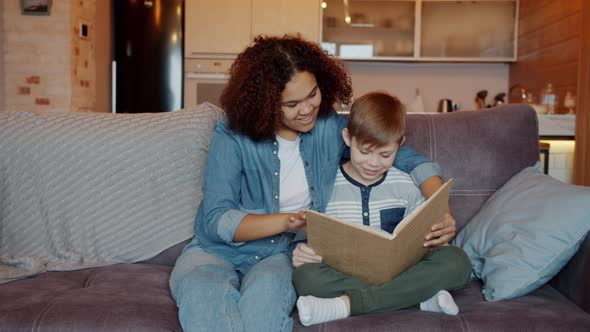 Afro-American Woman Babysitter Reading Book To Cute Little Boy at Home alt