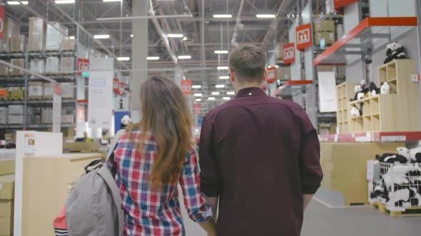 Young Couple Hold Hands in Large Store, Back View alt