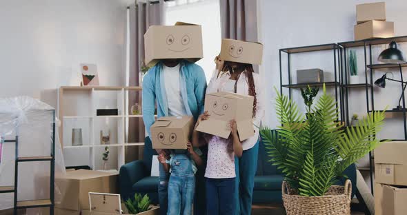 Modern Family with Two Small Kids Hiding their Heads Under Carton Boxes with Depicted Smiles alt