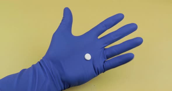 One Round White Pill in Hand Dressed in Rubber Sterile Medical Glove alt