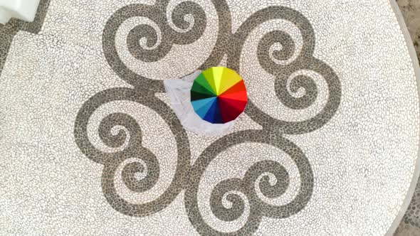 Aerial view of woman spinning rainbow umbrella in Santorini island, Greece. alt