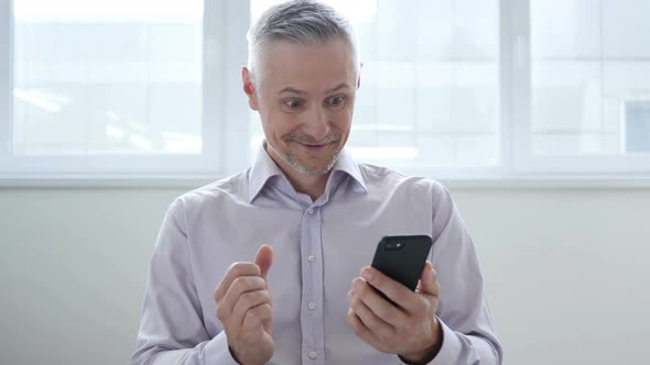 Middle Aged Man Excited for Success While Using Smartphone alt