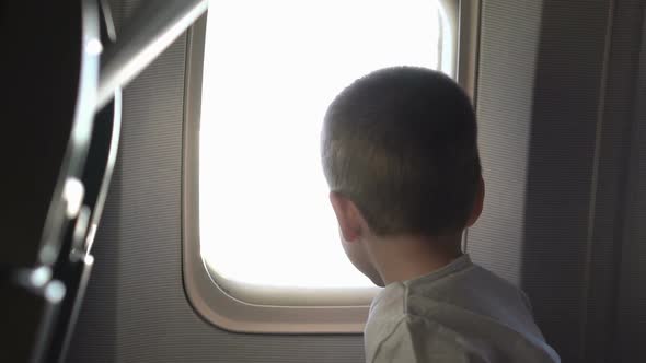 Young Cute Boy Sitting on the Seat and Opens Up Airplane Window alt