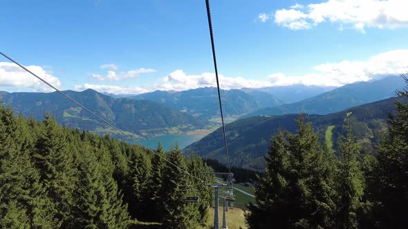 Sitting in a chair lift that goes down between tall spruce trees in the summer alt