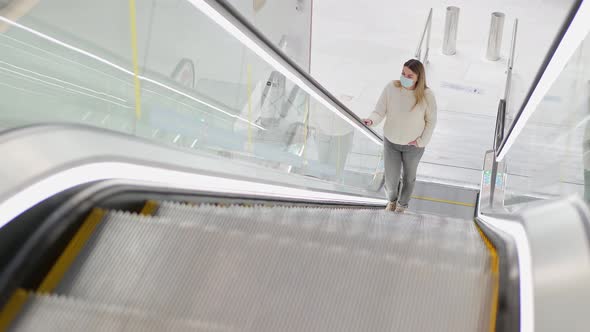 a Young Woman in a Protective Mask Climbs an Empty Escalator alt