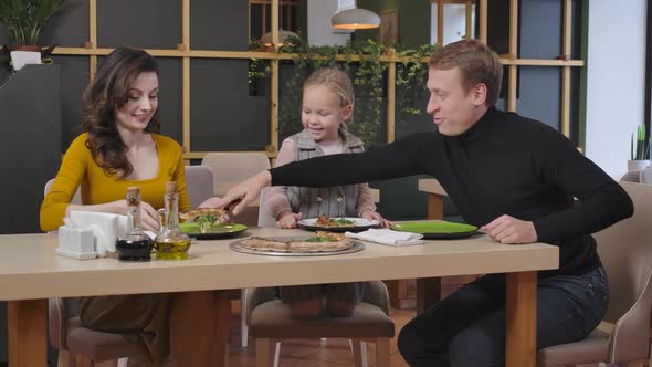 Cheerful Man Putting Pizza on Plates of Family in Restaurant alt