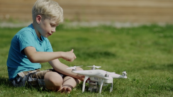 Child Assembling Modern Drone On The Green Grass Lawn. Putting On Propellers alt