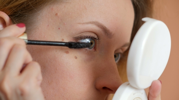 Young Girl Doing Makeup Of Eyes By Black Mascara, Looking At Small White Round Mirror 