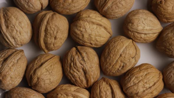 Cinematic, rotating shot of walnuts in their shells on a white surface  alt