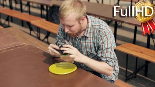 Man Eating a Black Burger at the Fair alt
