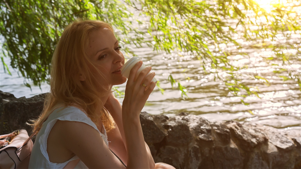Beautiful Girl Sitting Near Lake in City Park and Drinking Coffee 2