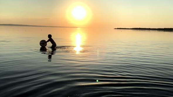 Children Playing Ball In The Water At Sunset.