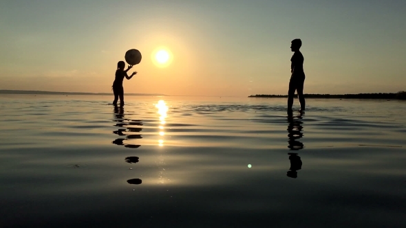 Children Playing Ball In The Water At Sunset.