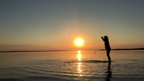 A Young Girl Splashes Water At Sunset