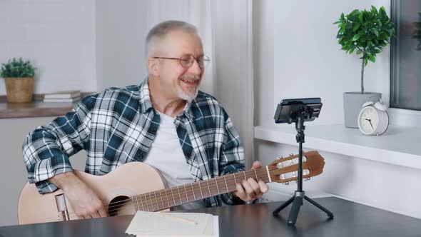 Smiling Middleaged Blogger Plays Guitar While Shooting Video on Smartphone